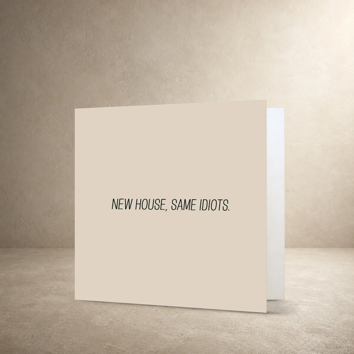 Minimal beige card front with a narrow centred typographic layout, with the message: “New house, same idiots.”.