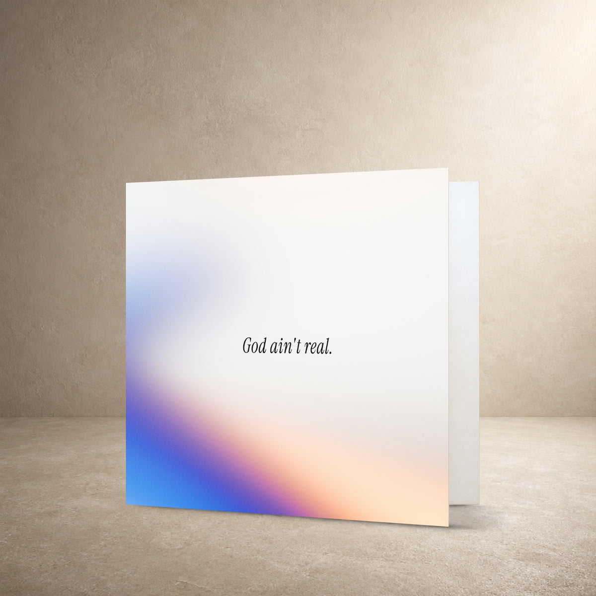 Minimal card front with a soft white background and blurred blue, purple and peach gradient, with the message: “God ain't real.”.