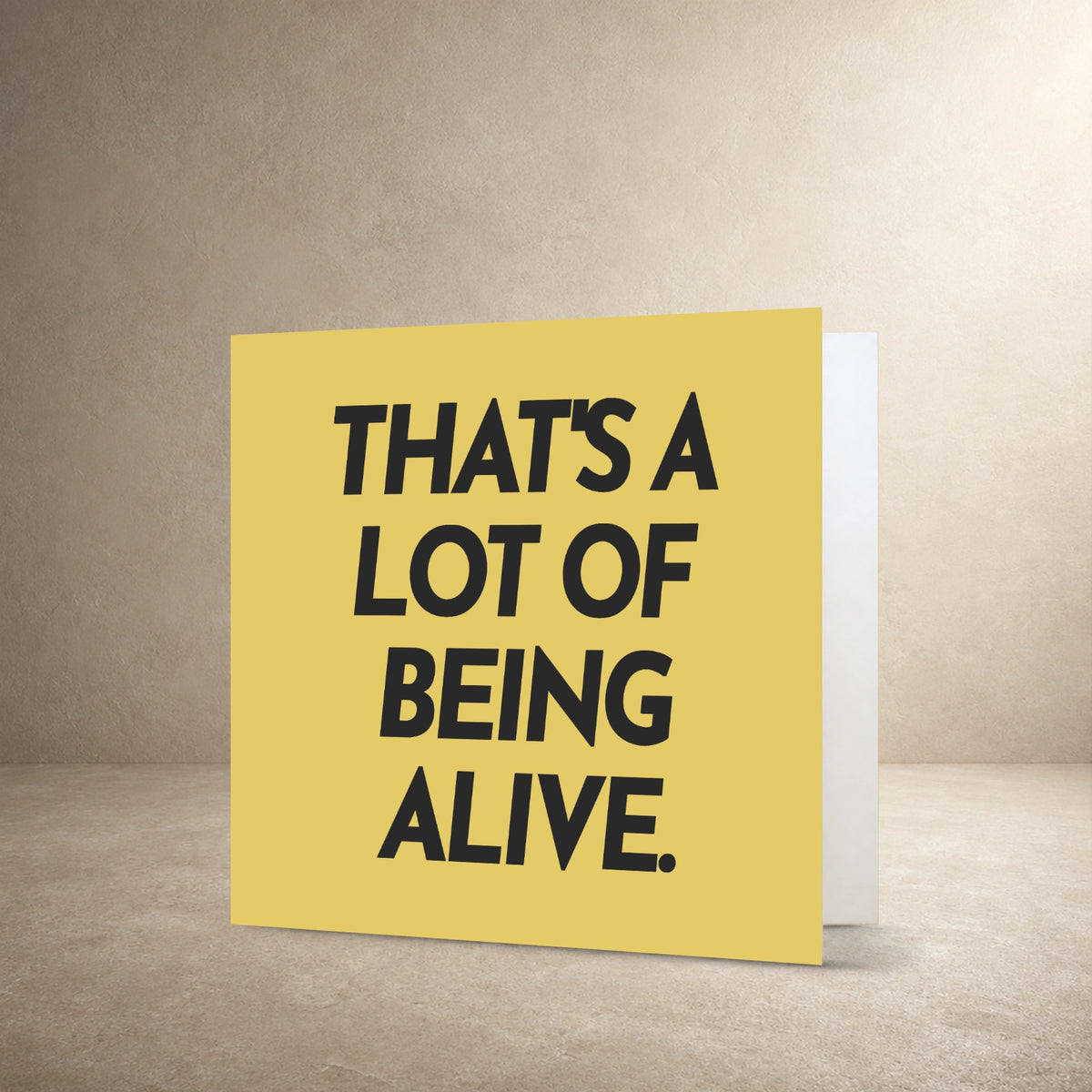 Mustard yellow card front with dark grey solid typography, with the message: “That's a lot of being alive.”.