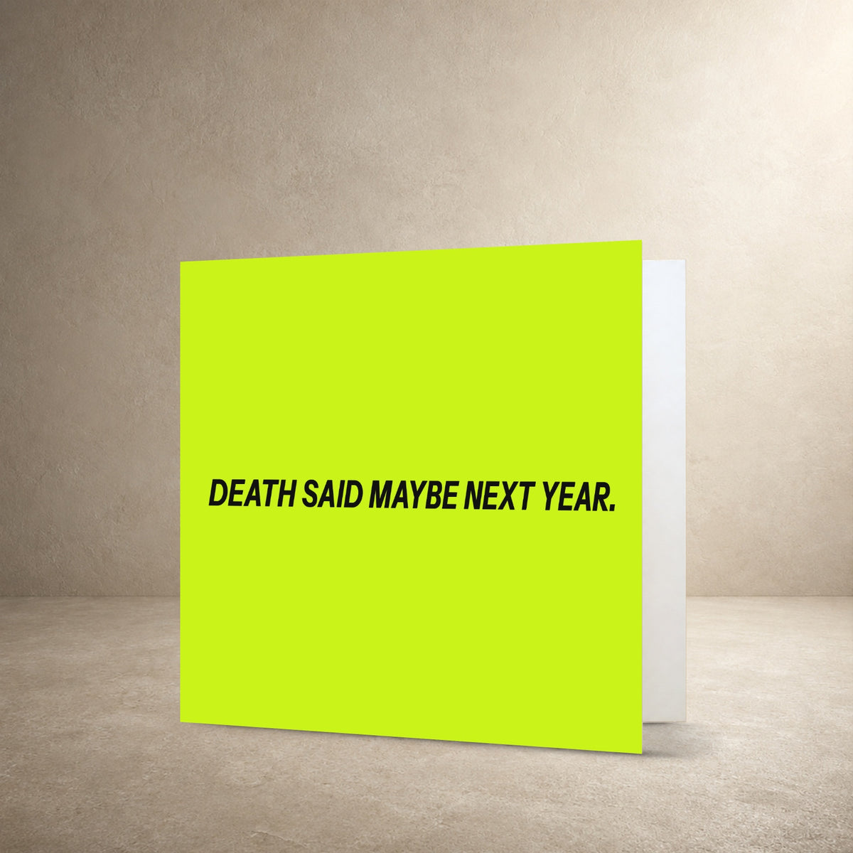 Minimal pale lime card front with bold dark centred typography, with the message: “Death said maybe next year.”.