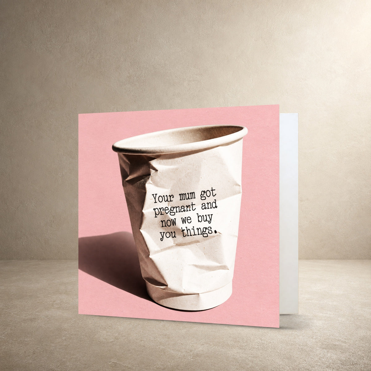 Crumpled white paper cup on a textured pink background, with the message: “Your mum got pregnant and now we buy you things.”.