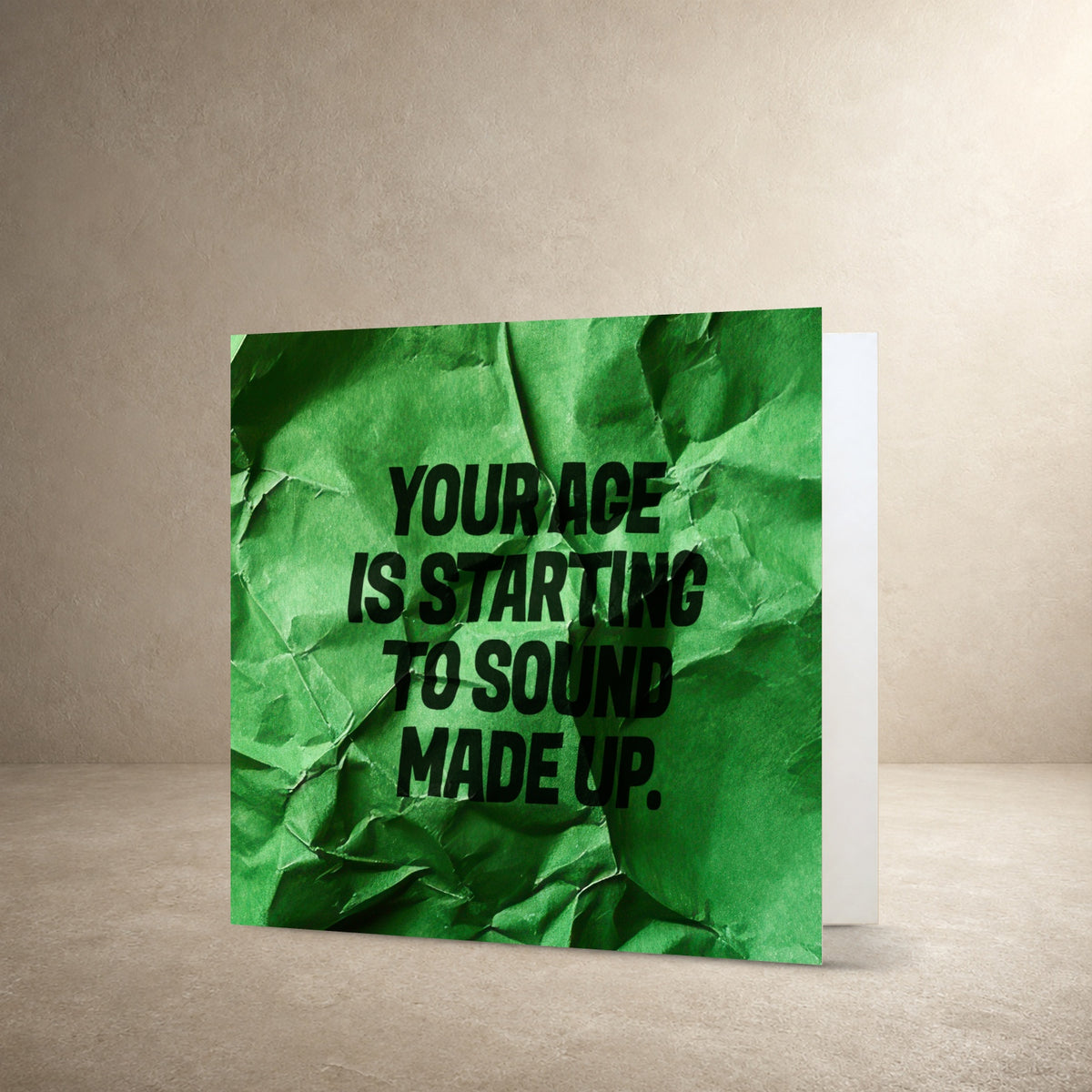 Bright green crumpled paper card front with realistic folds and texture, with the message: “Your age is starting to sound made up.”.