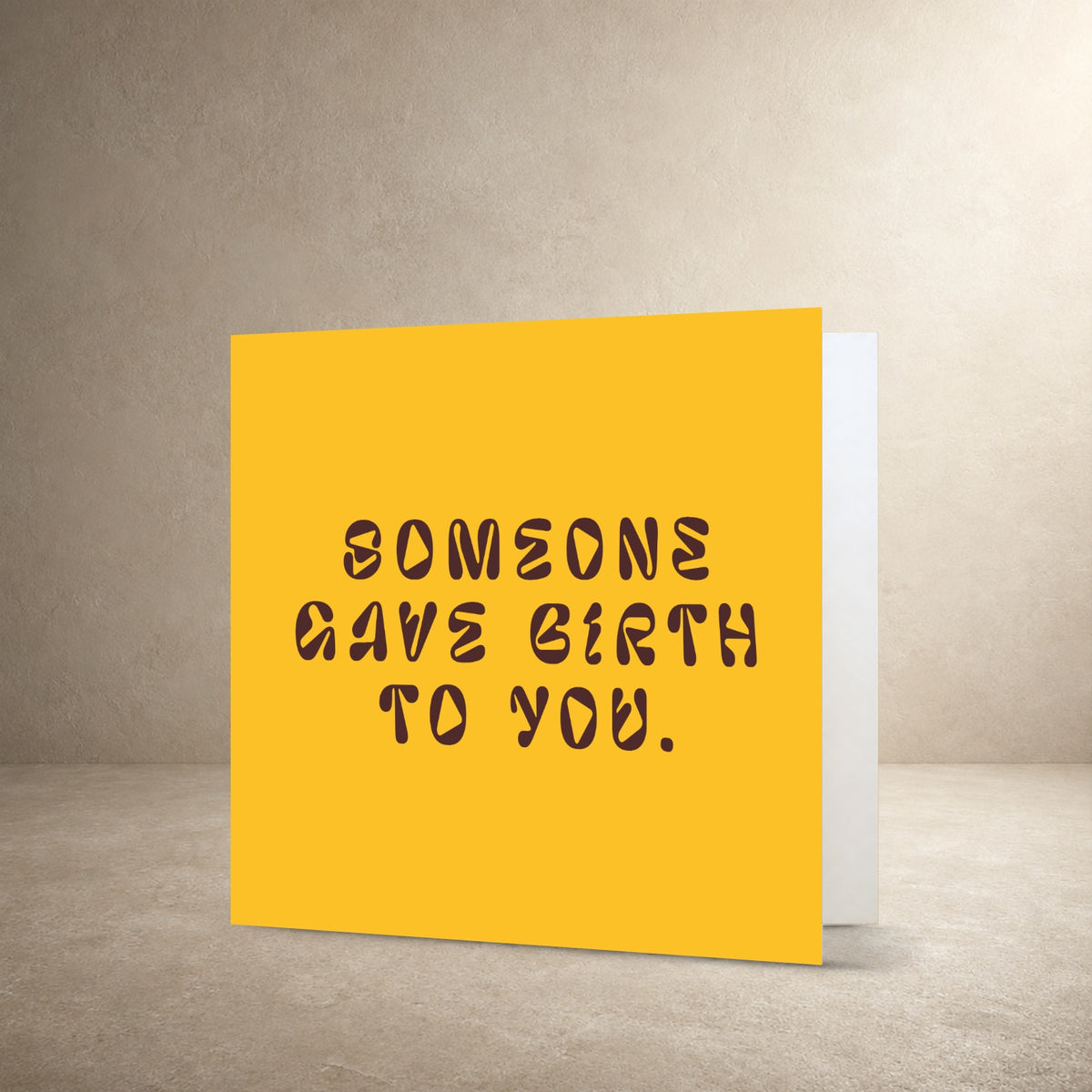 Golden yellow card front with dark brown typography, with the message: “Someone gave birth to you.”.